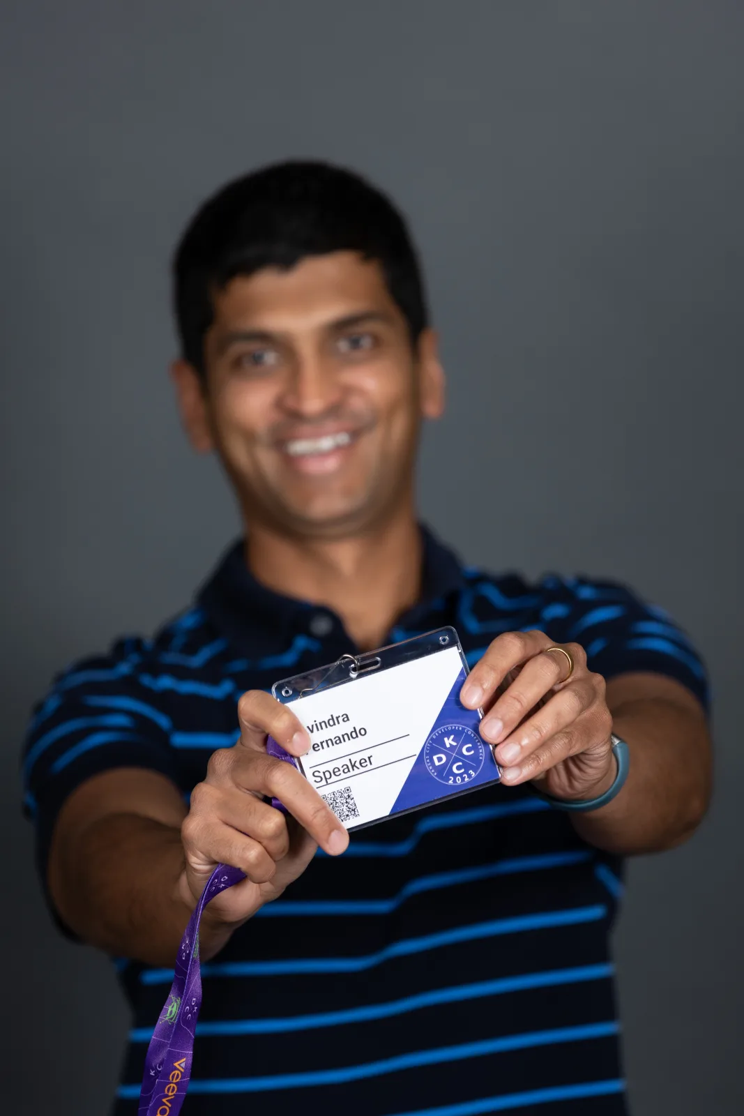 Avindra Fernando holding his KCDC 2023 speaker badge out to the camera