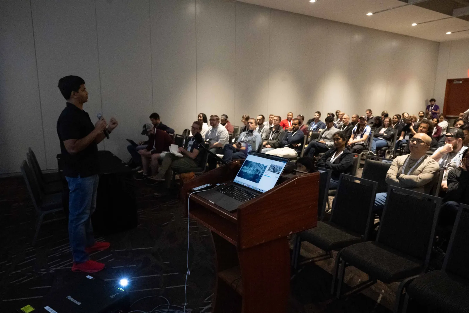 Avindra Fernando speaking to a packed conference room, mic in hand